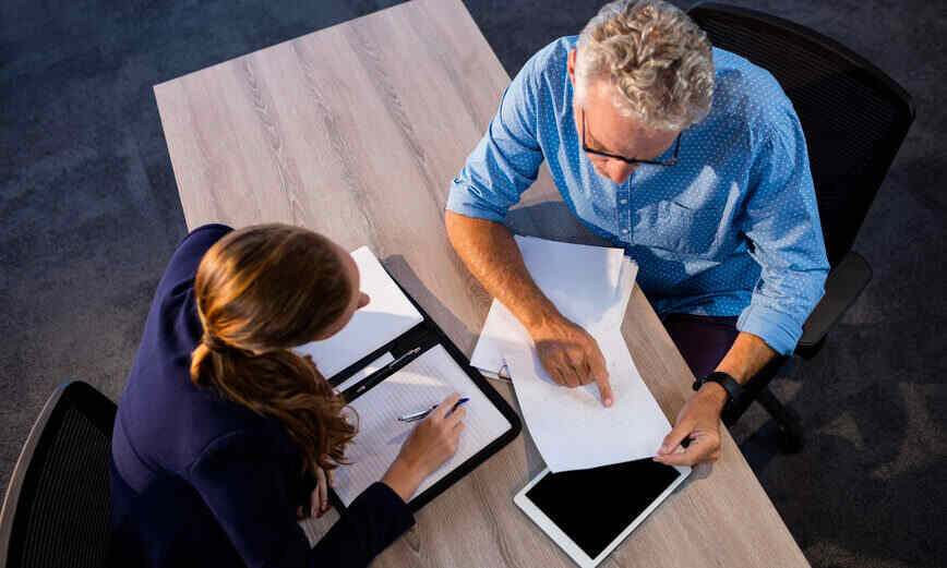 A man and woman are seated at a table, engaged with a tablet and pen, discussing ideas or taking notes.