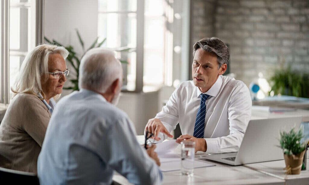 Financial advisor and senior couple talking while going through paperwork on a meeting.