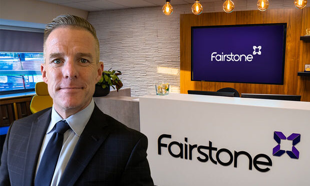 A man in a suit and tie stands confidently in front of a Fairstone logo, showcasing professionalism and brand identity.