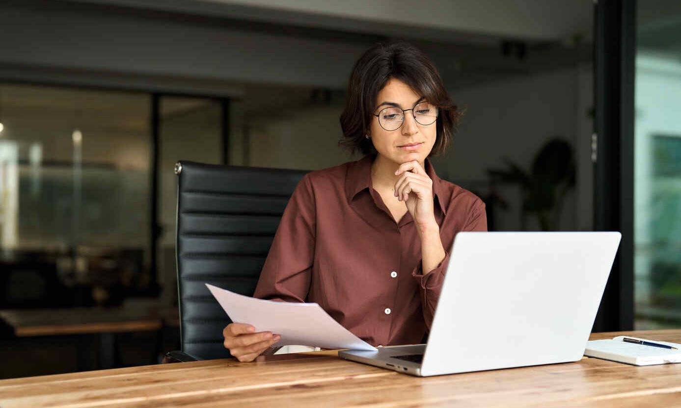 Busy serious young business woman manager working in office checking law document account invoice thinking in office. Businesswoman ceo executive or legal expert using laptop computer at work.