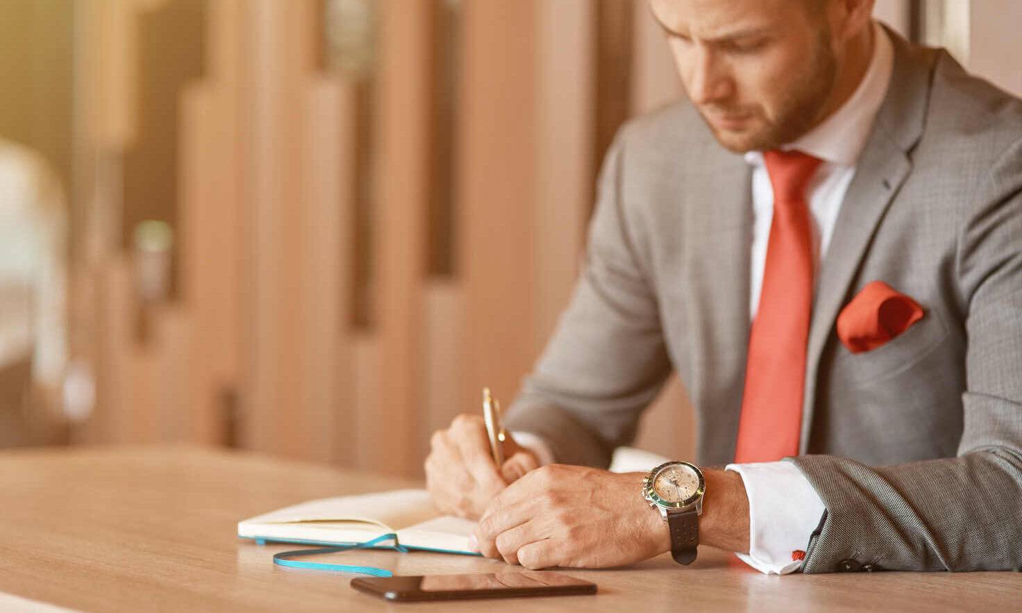 Serious professional businessman sitting at the table and making notes while being involved in work