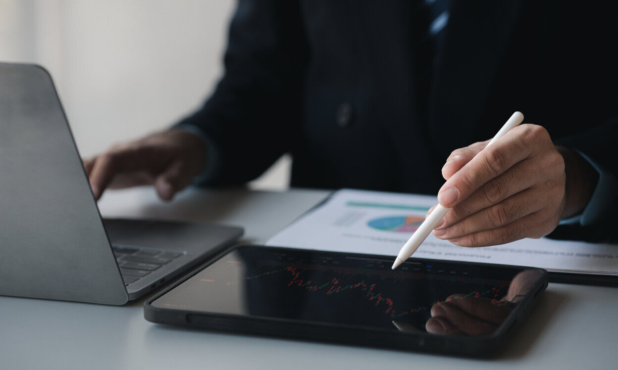 A man in a suit writes on a tablet with a pen about Stock price charts and stock market analysis, stock trading technology and digital assets, investors