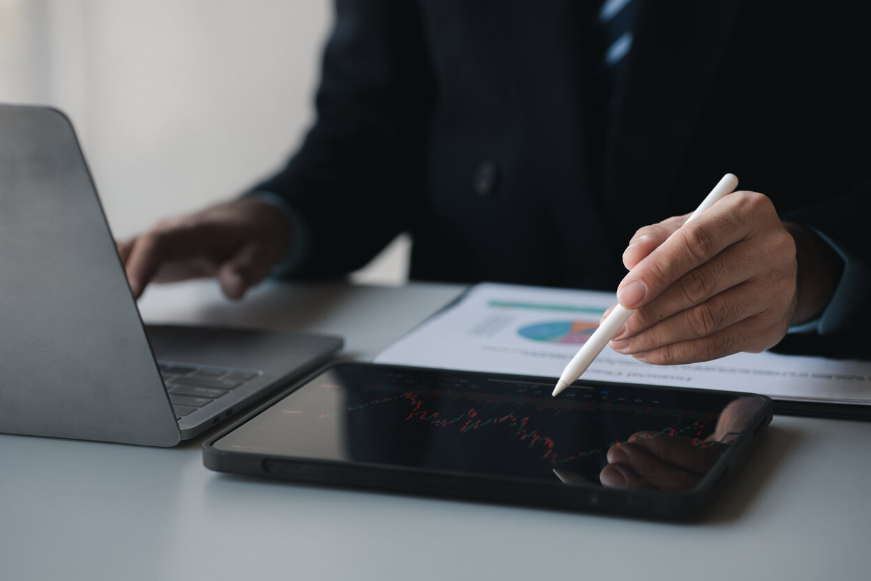 A man in a suit writes on a tablet with a pen about Stock price charts and stock market analysis, stock trading technology and digital assets, investors