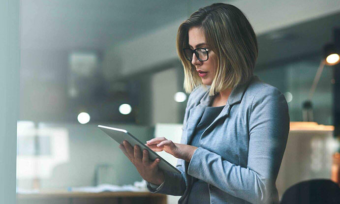 A woman wearing glasses is intently looking at a tablet screen, engaged in her digital activity.