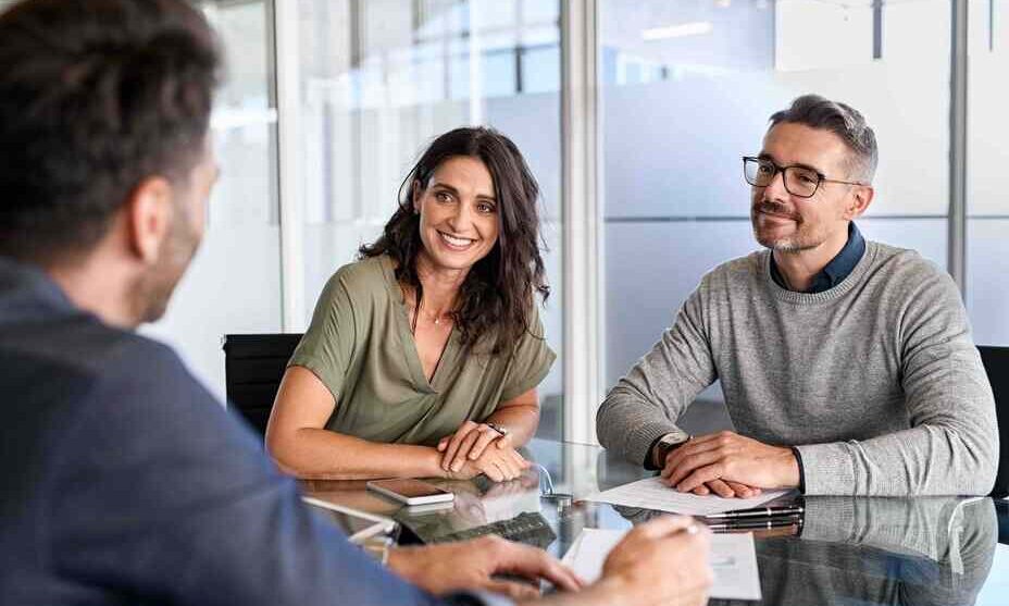 Smiling mature couple meeting with bank manager for investment. Beautiful mid adult woman with husband listening to businessman during meeting in conference room in modern office. Happy middle aged couple meeting loan advisor to buy a new home.