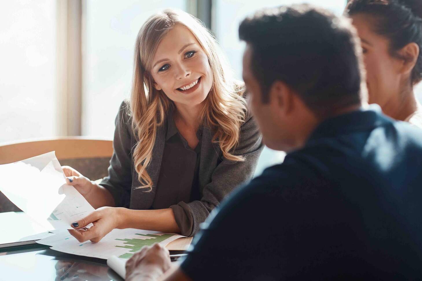 A female pension advisor engages in conversation with a young couple at a table about their finances.