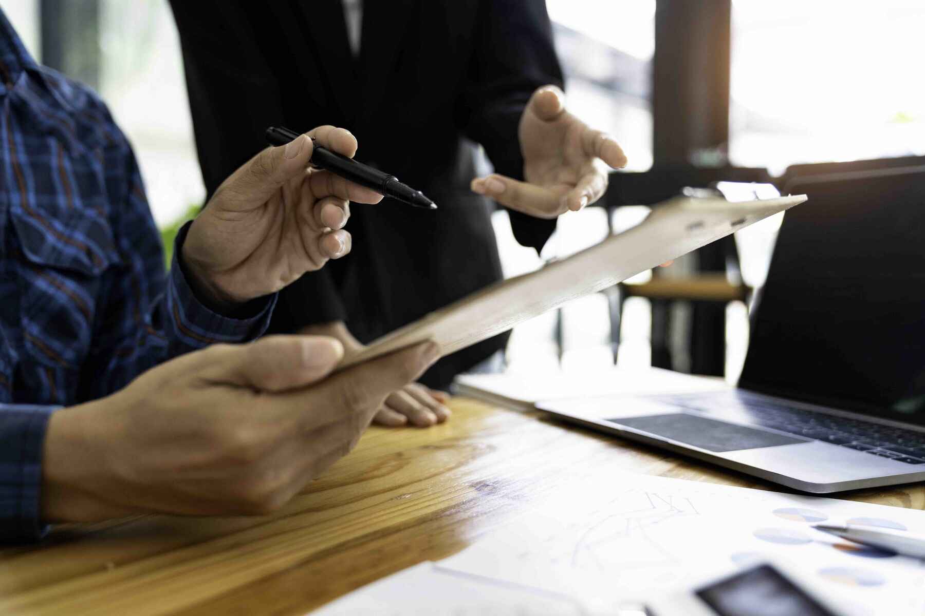 Two individuals collaborate on a laptop and clipboard, focused on their work in a professional setting.