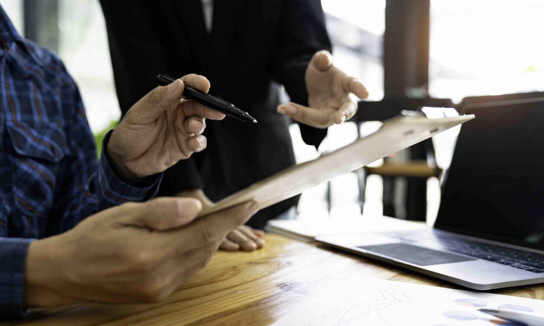 Two individuals collaborate on a laptop and clipboard, focused on their work in a professional setting.
