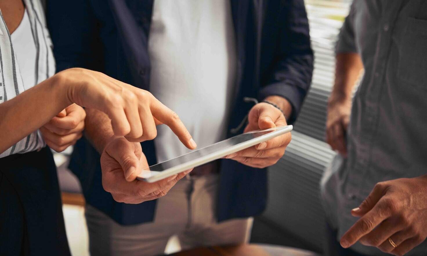 A diverse group of people gathered around a tablet computer, engaged in discussion and sharing ideas on how to track down an old pension.