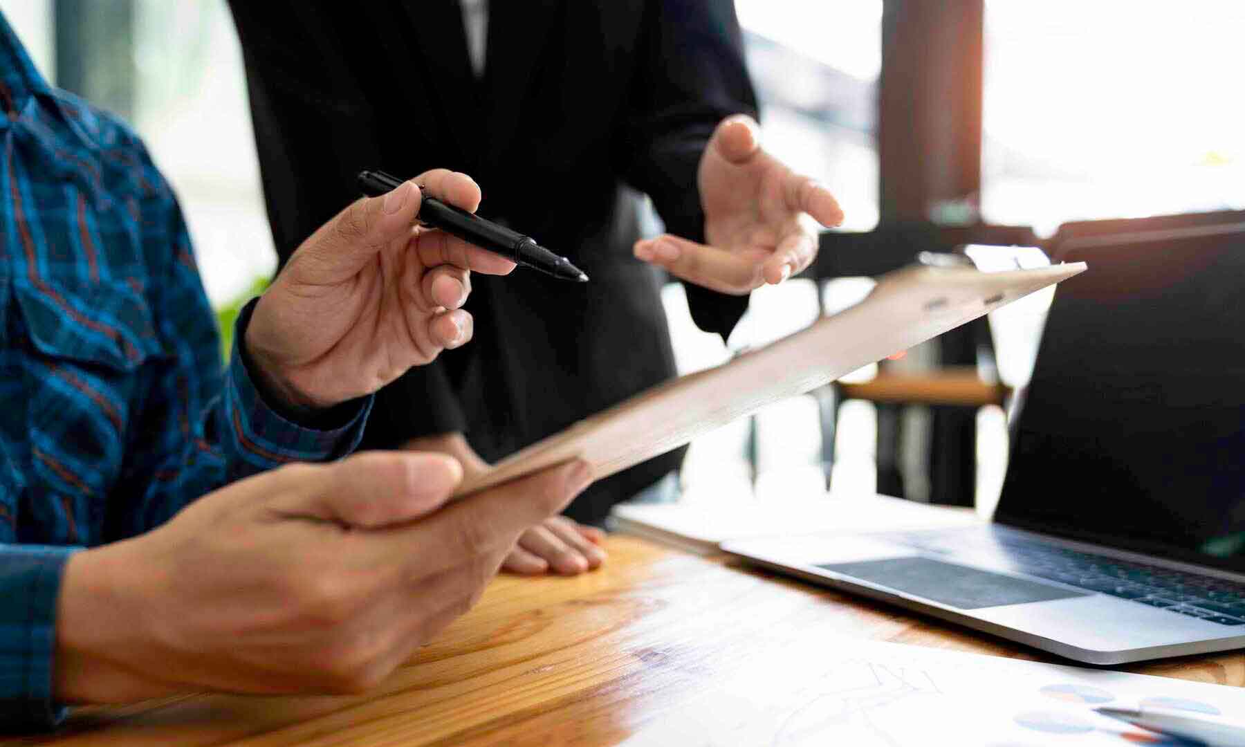 Pension consolidation - Two individuals collaborate on a laptop and clipboard, focused on their work in a professional setting.