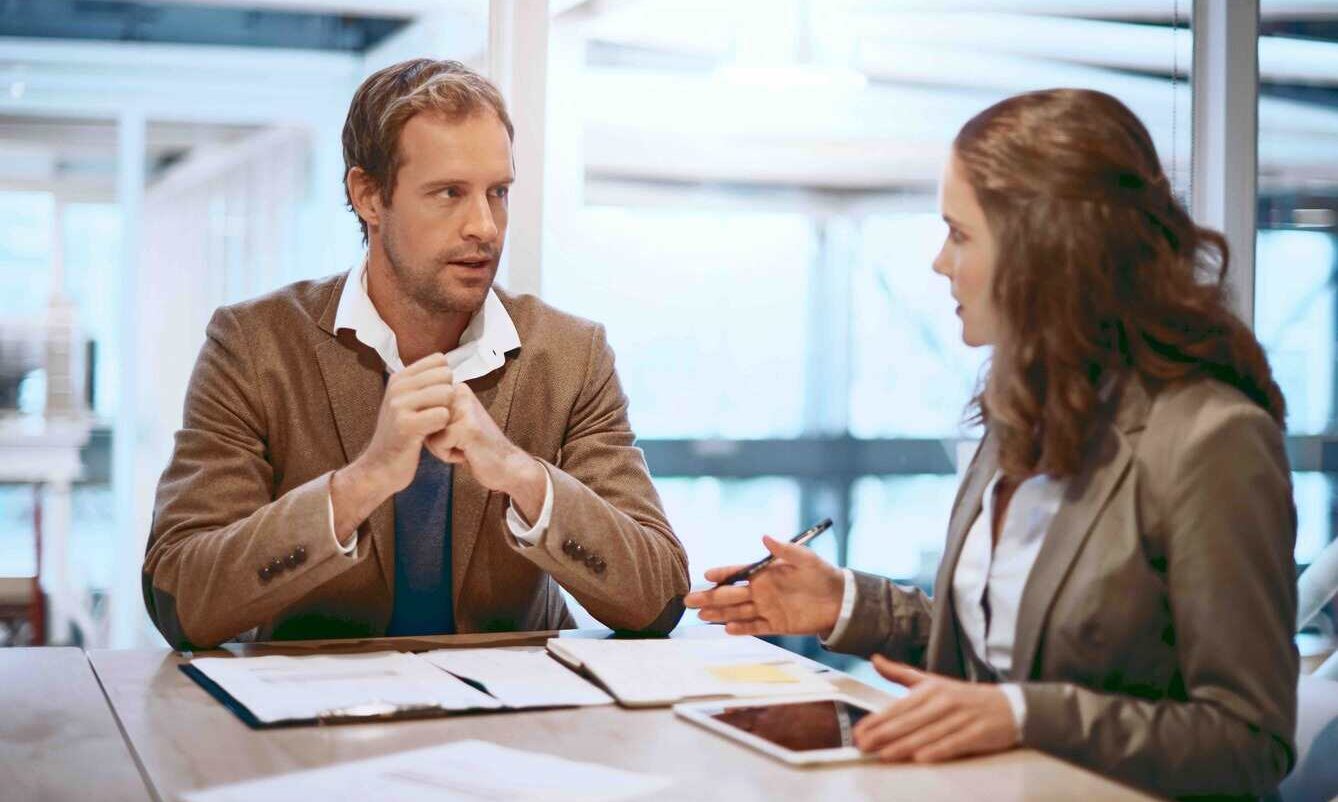 A man and woman sit at a table, reviewing documents and discussing details together.
