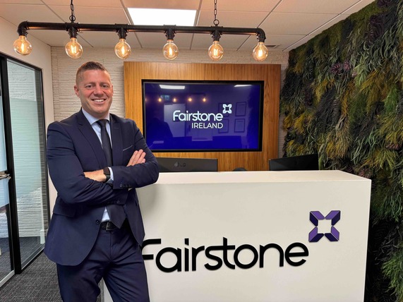 Derek Delany, Fairstone Ireland Managing Director standing at the front desk smiling and with folded arms with Fairstone logo in the background