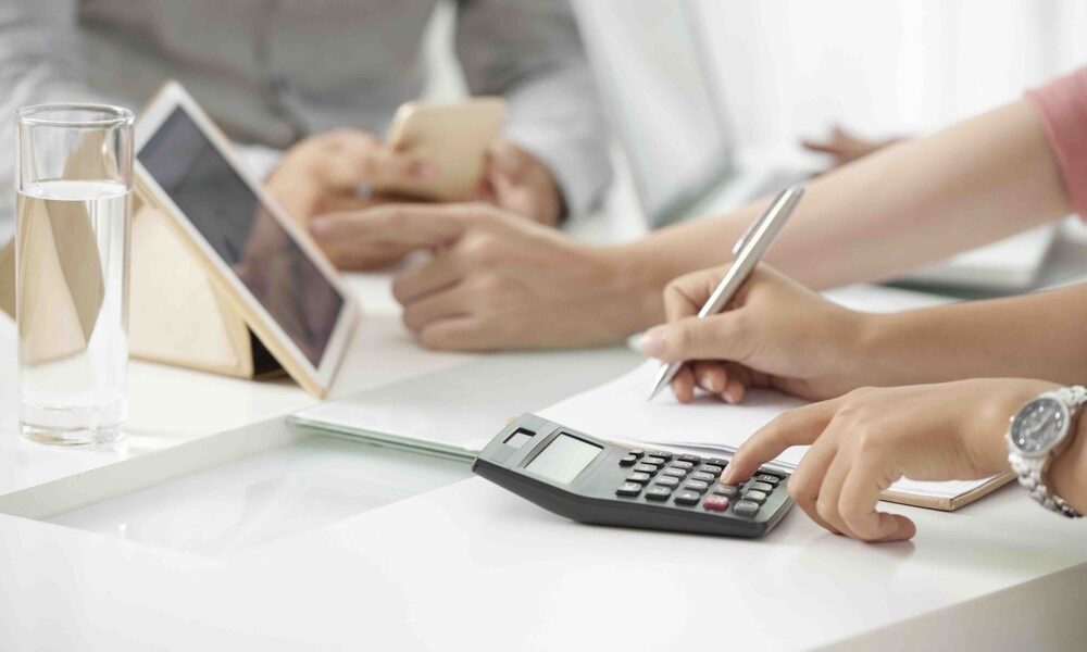 Understanding Capital Gains Tax in Ireland | Fairstone Ireland Crop shot of businesswoman using calculating machine and writing down numbers working with colleagues in office