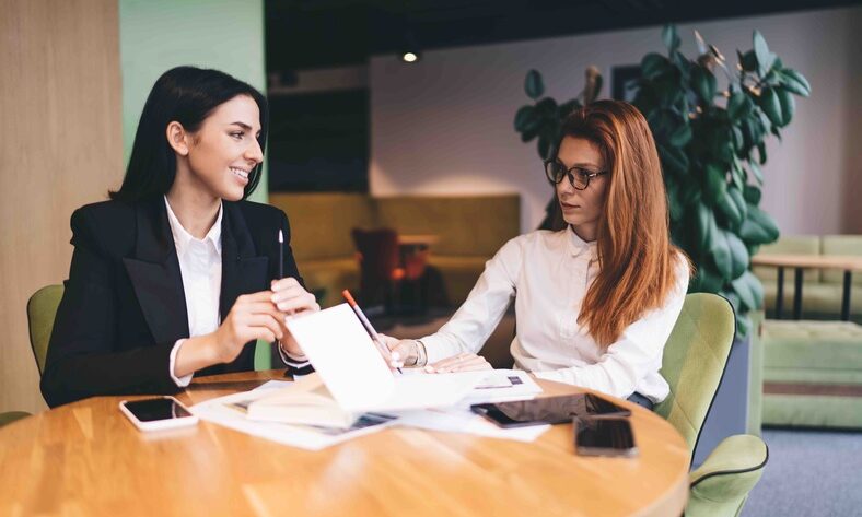 Two businesswomen engaged in discussion while seated at a table in a modern office setting, discussing what is an ARF.