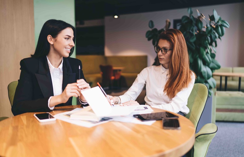 Two businesswomen engaged in discussion while seated at a table in a modern office setting, discussing what is an ARF.