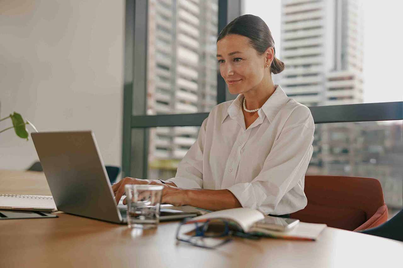 Best Savings Accounts in Ireland - A woman seated at a table, focused on her laptop, with a calm expression in a well-lit room.