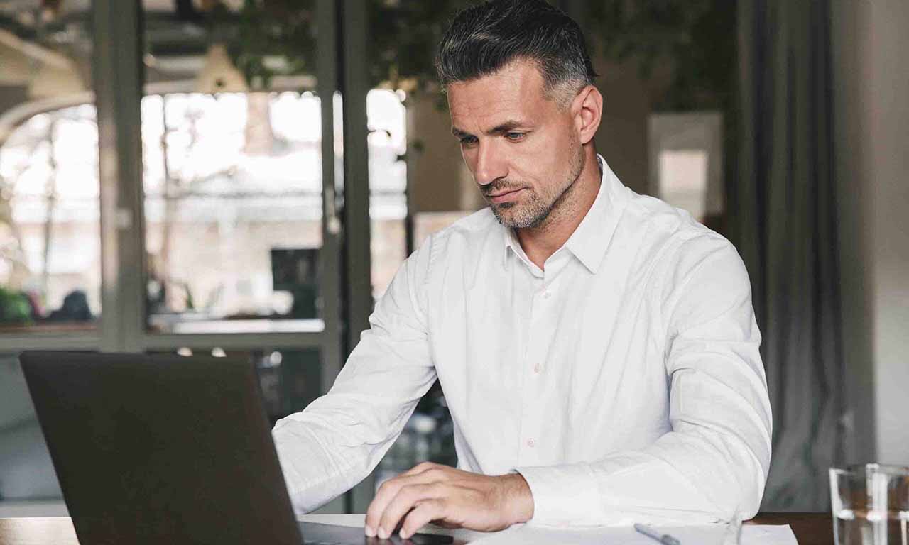 Budget 2026 - A man in a white shirt is focused on his laptop, working intently in a well-lit environment.
