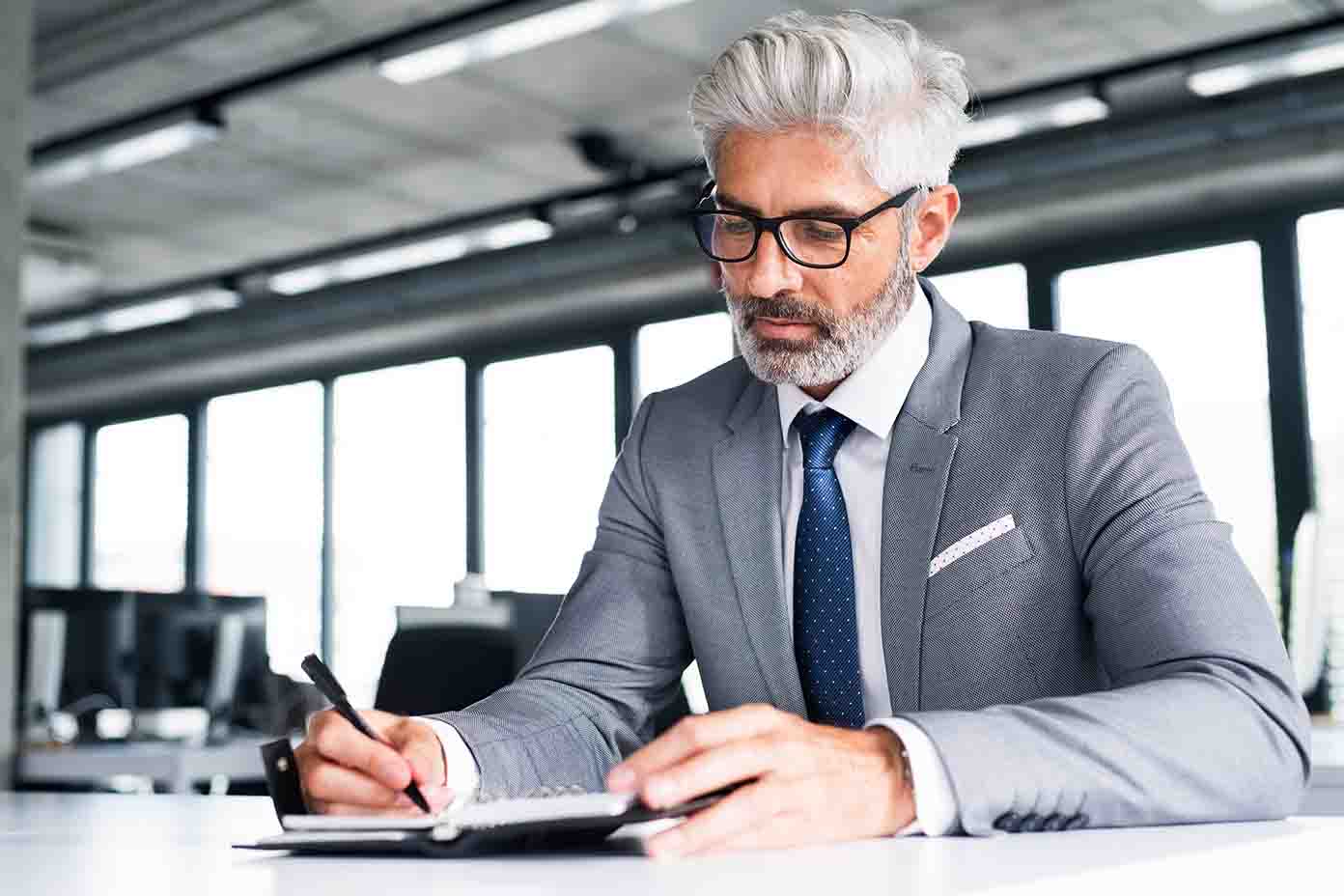Year-End Wealth Checklist - A man in a suit and glasses writes notes in a notepad, focused and engaged in his work.