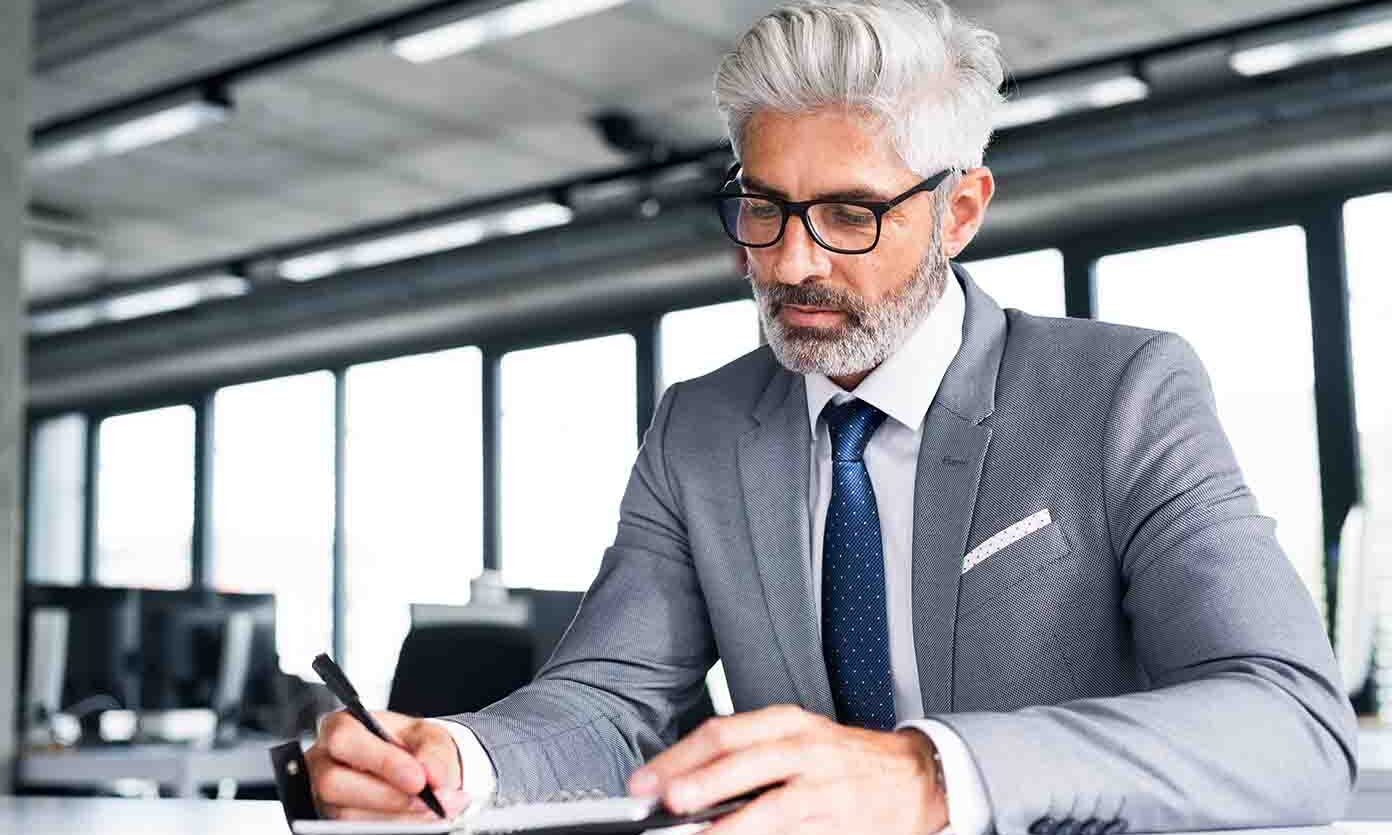 Year-End Wealth Checklist - A man in a suit and glasses writes notes in a notepad, focused and engaged in his work.