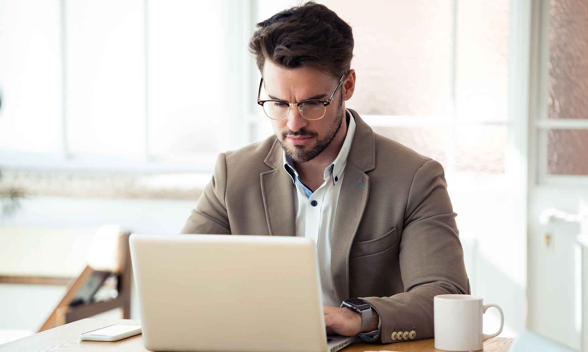 A man in a suit is focused on his laptop, working intently in a professional setting.