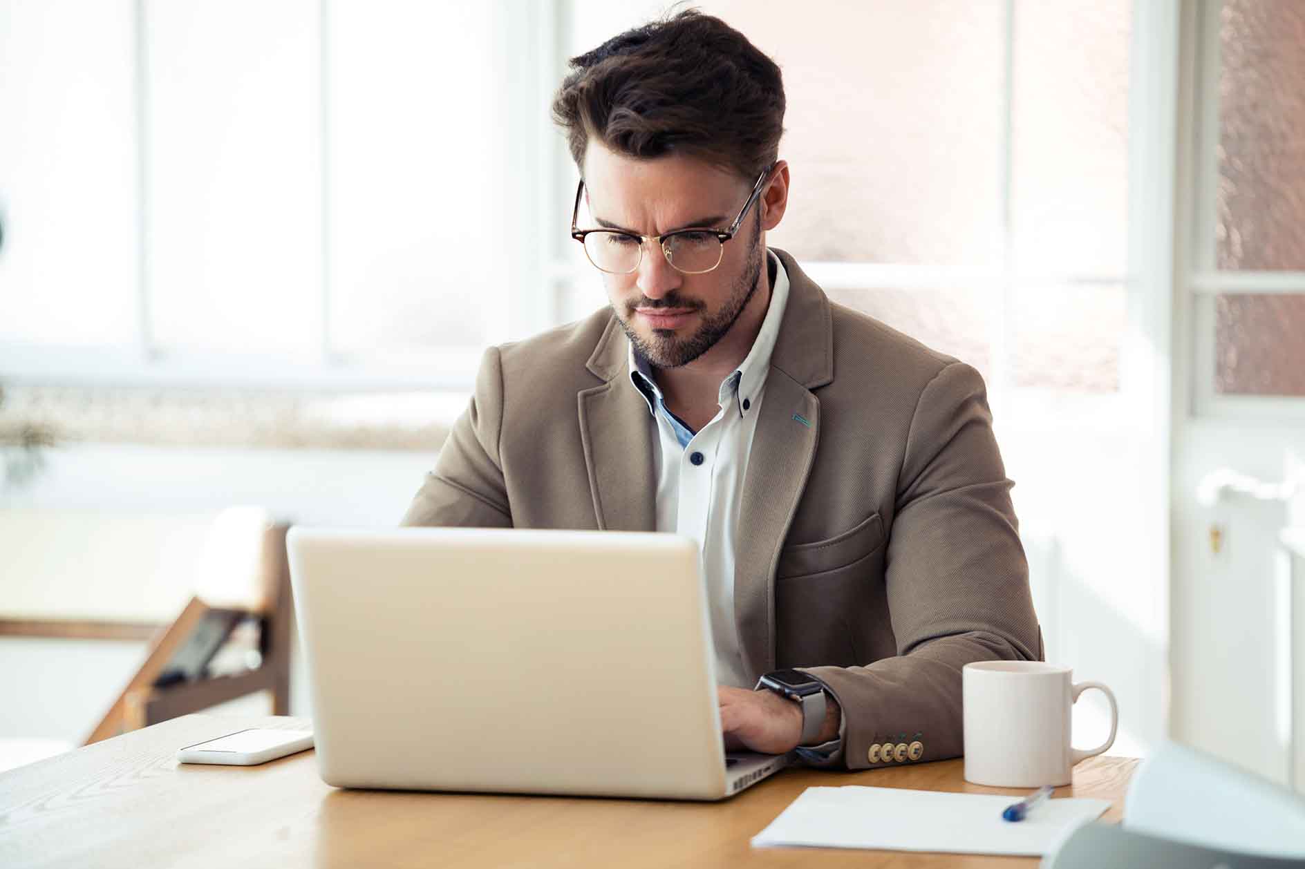 A man in a suit is focused on his laptop, working intently in a professional setting.