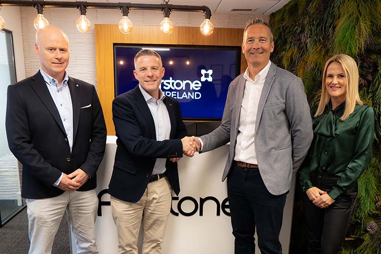 A group of three men and a women shake hands in front of a TV, representing teamwork and partnership.